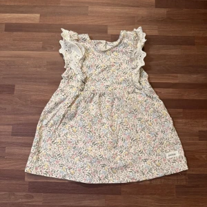 Blommig klänning - Supersöt klänning från Newbie i storlek 74 (4-6mån) med blommigt mönster i pastellfärger. Använt två gånger och är i nyskick. Knappar i ryggen. Bortklippt tvättråd. Har en dubblett av denna med tvättrådet kvar. Kan köpas som set med två andra klänningar, till paketpris. Säljes separat på min profil.