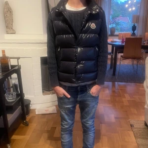 Marinblå väst från Moncler - Snygg marinblå Moncler tib dunväst med glansig finish. Västen har hög krage, dragkedja och knapp knäppning framtill och Moncler-logga på bröstet. Perfekt för kyliga dagar när du vill ha både stil och värme.                                                   Självklart äkta❗️❗️                                             Några frågor? Slå en pling 🛎️❗️