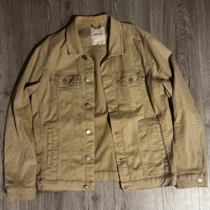 Beige overshirt  från Jack & Jones - Snygg beige jeansjacka från Jack & Jones med klassisk krage, knappar framtill och två bröstfickor med lock. Jackan har raka linjer och är perfekt för dig som gillar enkel och stilren design. Passar till många olika outfits och har en cool streetkänsla.