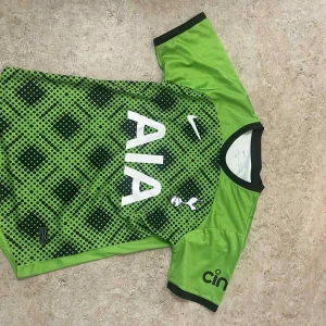 Grön Tottenham Hotspur fotbollströja - Snygg grön Tottenham Hotspur fotbollströja från Nike med svart och mörkgrönt prickigt mönster på framsidan. Stor vit AIA-logga, klubbmärke och Nike-swoosh på bröstet. Svarta detaljer vid krage och ärmslut. Tillverkad i lätt och ventilerande polyester.
