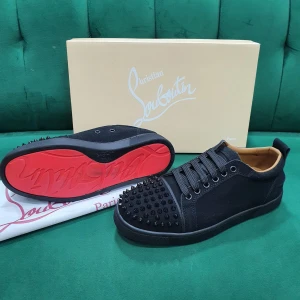 Svarta sneakers från Christian Louboutin - Snygga svarta sneakers från Christian Louboutin med ikonisk röd sula och svarta nitar på tån. Skorna har snörning och en rund tå, tillverkade i skinn och textil. Perfekt för dig som vill sticka ut med en edgy och lyxig stil.