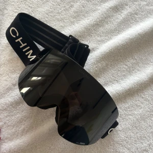 CHIMI Svarta skidglasögon - Säljer ett par svarta skidglasögon från CHIMI med Zeiss-lins. De har en bred, mörk och spegelblank lins med minimalistisk design och svart elastiskt band med vit CHIMI-logga. Perfekt för dig som vill ha stilrena goggles i backen. De är använda under två veckor totalt och har inga större tecken på användning. Bra skick! Skriv för fler bilder eller frågor💕