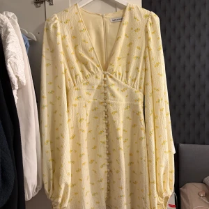Adoore blommig gul klänning - Supersöt ljusgul klänning från Adoore med små gula blommor, v-ringning och klädda knappar framtill. Klänningen är använd 2 gånger så är fortfarande i toppen skick. 