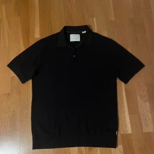 Mörkblå pikétröja från Jack & Jones - Klassisk Mörkblå pikétröja från Jack & Jones med krage och två knappar framtill. Tröjan har korta ärmar och är tillverkad i mjukt stickat material som ger en clean och stilren look. Perfekt för dig som gillar enkel och tidlös stil.