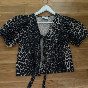 Leopardmönstrad blus med puffärm  - Säljer en snygg blus från neo nior med leopardmönster i svart och beige. Blusen har korta puffärmar, v-ringning och knytband framtill.