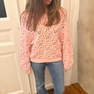 Rosa stickad tröja med ballongärmar - Superfin rosa stickad tröja med coolt virkat mönster och breda ballongärmar. Tröjan har en loose fit och är perfekt för dig som vill ha en mysig men ändå trendig look. Ribbstickade muddar vid ärmslut och nederkant. Så söt till jeans eller kjol!