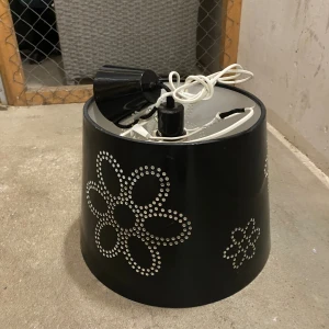 Svart taklampa med blommönster - Stilren svart taklampa med dekorativt blommönster i perforerat mönster. Mindre bruksspår och lite slitage på insidan, men i gott skick. Perfekt för vardagsrum eller sovrum.