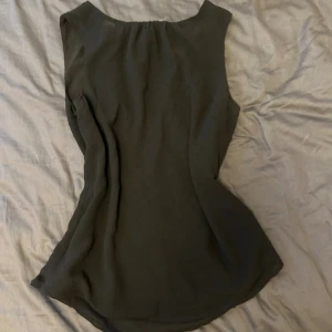 Svart prickig blus från H&M - Svart blus från H&M i storlek 34. Toppen är ärmlös med diskreta prickar i tyget och har en snygg omlott-detalj i ryggen med knytband upptill. Lätt och luftig modell som passar perfekt till jeans eller kjol.