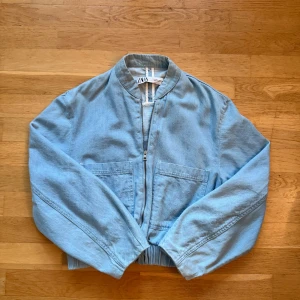 Ljusblå jeansjacka från Zara - Säljer en ljusblå jeansjacka från Zara med dragkedja framtill, två stora fickor och elastisk nederkant. 