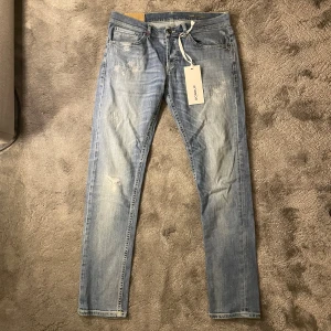 Dondup jeans - Snygga ljusblå skinny fit jeans från Dondup George med slitna detaljer och klassisk femficksdesign. Jeansen har orange kontrastsömmar, logotyp på bakfickan och en cool tvättad look. Perfekt för dig som gillar en smal siluett och streetstyle.