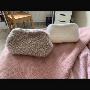 Beige stickad kuvertväska med blommönster - Superfin beige kuvertväska med stickat blommönster, perfekt att ha till mobilen och småsaker. Väskan är handgjord i mjukt ullgarn och har en fluffig, mysig känsla. Den har en rektangulär form och stängs med en enkel öppning upptill.