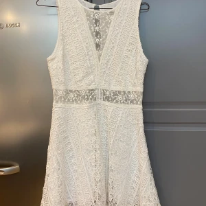 Abercrombie & Fitch vit klänning, storlek M - Supersöt vit kortklänning från Abercrombie & Fitch med spets och blommiga meshdetaljer vid midjan och bröstet. Ärmlös modell med v-ringning och dragkedja i sidan. Perfekt för student eller sommarens alla tillfällen. Sitter snyggt med normal passform.