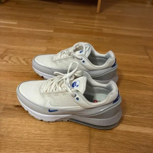 Nike Air Max vita sneakers strl 42 - Nike Air Max sneakers i vitt med grå och blå detaljer. Skorna har en luftig mesh-ovandel, klassisk snörning och synlig Air Max-dämpning i sulan. Snygg sportig look med diskret Nike-logga på sidan och AIRMAX-tryck bak. Perfekta för dig som gillar stilrena och bekväma sneakers.