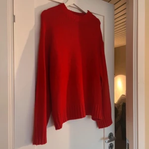 Röd stickad tröja från NA-KD - Säljer en snygg röd stickad tröja från NA-KD i storlek S. Tröjan har rund hals, långa ärmar och breda ribbade muddar vid ärmslut och nederkant. Perfekt för dig som gillar färg och vill ha en enkel men stilren look.