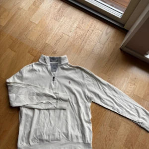 Vit half zip tröja från Polo Ralph Lauren - Snygg vit långärmad tröja från Polo Ralph Lauren med half zip och broderad logga på bröstet. Tröjan är gjord i mjuk bomull och har en klassisk, normal passform. Perfekt för dig som gillar stilrena och tidlösa plagg. Orginalpris: 2200kr. Modellen är 173cm lång och väger cirka 70kg.