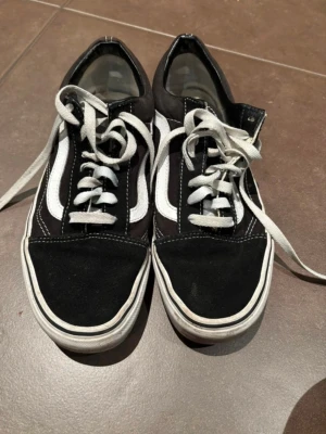 Svarta och vita Vans Old Skool sneakers - Klassiska Vans Old Skool sneakers i svart och vitt med vit sula och ikonisk sidorand. Skorna har snörning, rund tå och ovandel i mocka och canvas. Perfekta för en avslappnad streetstil och passar till det mesta i garderoben.