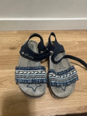 Girls Blue Sandals - Cute girls’ sandals in blue tones with decorative woven and beaded front strap. Comfortable soft leather footbed and adjustable velcro straps around the ankle for a secure fit. ✔ Brand: Tom Tailor ✔ Size: EU 32 ✔ Material: Soft leather insole ✔ Color: Blue / Navy ✔ Condition: Good used condition – normal signs of wear (see photos), still plenty of life left ✔ Perfect for: Summer, school, holidays, everyday wear From a smoke-free home. Feel free to message me if you have any questions 😊 
