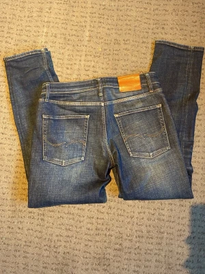 Blå jeans från Jack & Jones - Snygga blå jeans från Jack & Jones i klassisk femficksmodell. Jeansen har en rak passform med normal midja och slitna detaljer framtill. Materialet är robust denim med kontrastsömmar och läderpatch bak i midjan. Perfekt för dig som gillar en tidlös jeanslook.