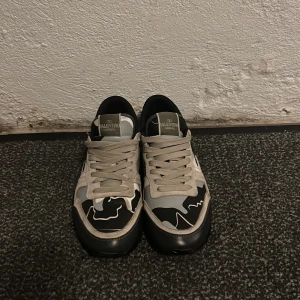Valentino Garavani Rockrunner sneakers - Säljer ett par Valentino Garavani Rockrunner sneakers med grå, beige och svarta toner. Skorna har ett snyggt camouflage-mönster, rund tå och platt sula. Ovandelen är i mocka och skinn med snörning och coola detaljer på hälen.