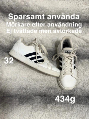 Adidas sneakers vita med svarta ränder - Säljer ett par klassiska Adidas sneakers i storlek 32. Skorna är vita med svarta ränder på sidorna och har snörning framtill. Perfekt för dig som gillar sportig stil.🌸 Använda och därav mörkare på vissa ställen efter användning. Ej tvättade men avtorkade. Storlek 32
