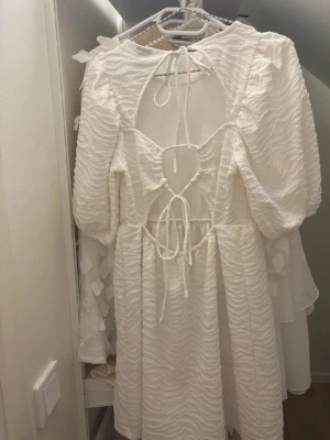 Vit kortklänning från Gina Tricot - Supersöt vit kortklänning från Gina Tricot i storlek S. Klänningen har puffiga långärmar, ett vågigt strukturerat tyg och snygga snörningsdetaljer med öppen rygg. Perfekt för dig som gillar trendiga detaljer och en feminin look. Jag har bara använt den en gång på skolavslutningen. Pris kan sänkas vid snabb affär
