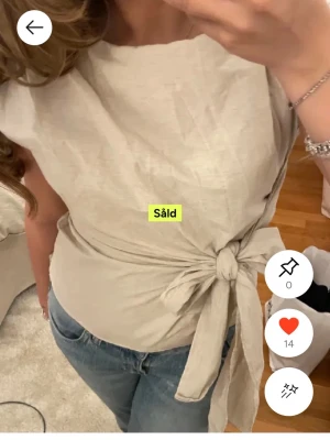 Beige omlottopp med knyt - Säljer en stilren beige omlottopp med knyt i sidan. Toppen är ärmlös och har en mjuk, naturlig linnekänsla som gör den enkel att matcha med jeans eller kjol. Perfekt för dig som gillar minimalistisk och fräsch stil. Om ni vill ha egna bilder är det bara att fråga 