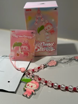 PopMart Labubu Big Into Energy Phone Charm - Love - Otroligt fint smycke för mobil, väska eller nyckelring. Rött och rosa med skimrande berlocker. Smycket håller hög kvalitet, väldigt hållbar då den inte är elastisk.  Smycket är helt nytt, detaljer och kort är fortfarande förseglat.