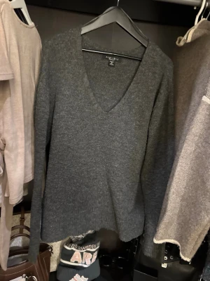 Mörkgrå stickad tröja från Amisu - Mysig mörkgrå stickad tröja från Amisu med v-ringad hals och lång ärm. Perfekt för kyliga dagar och enkel att matcha med jeans eller kjol. Tröjan har en loose passform och känns riktigt skön mot huden.