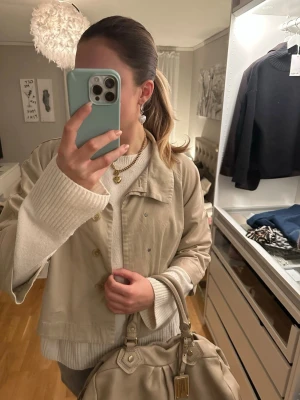 Beige trenchcoat med 3/4 armlängd - Snygg beige trenchcoat från Mexx. Perfekt att slänga över en hoodie eller stickad tröja. Enkel och stilren design som funkar till det mesta. Storlek saknas men skulle säga att den passar S/M. Köptes på vinted för 500kr