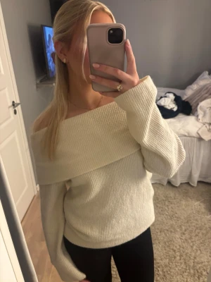 Offshoulder stickad tröja i vitt - Superfin offshoulder stickad tröja i vit färg. Tröjan har bred krage som sitter snyggt över axlarna och långa ärmar. Perfekt till höst och vinter, och passar till både jeans och kjol. Mjuk och skön med ribbad struktur.