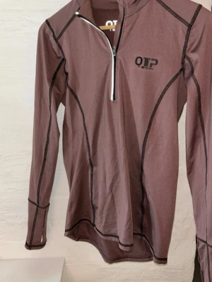 Träningströja - Långärmad träningströja i lila med svarta sömmar och reflexer. Mjukt tyg i flis med dragkedja och långa ärmar med hål för tummen. Varm vid träning eller promenad utomhus eller som underställ.