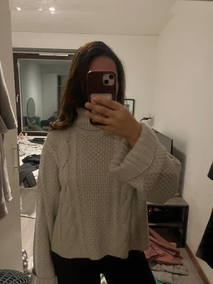 Beige stickad polotröja med flätmönster - Säljer en beige stickad polotröja med breda ärmar och snyggt flätmönster framtill. Tröjan har hög krage och är riktigt mysig och oversized, perfekt för kyliga dagar. Passar dig som gillar en chill och trendig look.