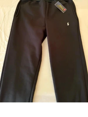 Svarta mjukisbyxor Polo Ralph Lauren - Svarta mjukisbyxor från Polo Ralph Lauren med broderad logga på benet. Byxorna har resårmidja med snörning och sidofickor. Tillverkade i mjukt material som känns skönt mot huden. Perfekta för chill dagar eller när du vill ha det bekvämt. Inte stora!! 