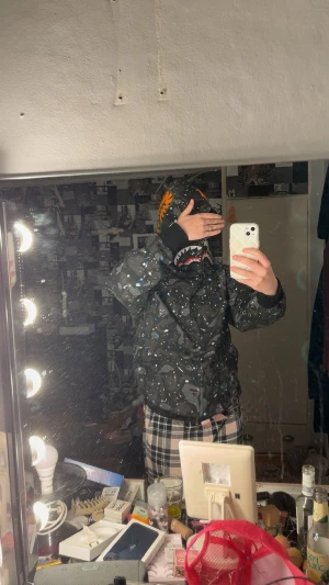 BAPE Shark Camo vindjacka svart M - Säljer en svart BAPE Shark Camo vindjacka med ikonisk hajhuva, broderade detaljer och färgglada bokstäver på huvan. Jackan har dragkedja, camomönster med blå och vita stänk samt ribbade muddar. Perfekt för dig som vill sticka ut med streetwear-vibe. Helt äkta. Nypris 7000