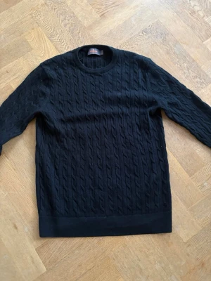 Svart kabelstickad tröja Morris - Kabelstickad svart tröja från Morris i 100% merinoull. Klassisk rund halsringning och långärmad modell. i storlek M/S. Snygg struktur med kabelmönster över hela tröjan, perfekt för kyligare dagar. Priset kan diskuteras vid snabb affär. 