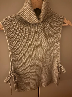Trendig Beige stickad polotröja  - Stickad beige polotröja från Indiska med grov ribbad struktur och höga sidor med knytband. Tröjan är ärmlös och har en bred, mysig polokrage. Superskön och inte alls stickig! Skriv privat för mer information!