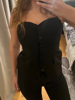 Svart korsett-topp  - Säljer en svart korsett-topp i storlek M. Toppen är axelbandslös med snygga stora knappar framtill och två dekorativa fickor!❤️