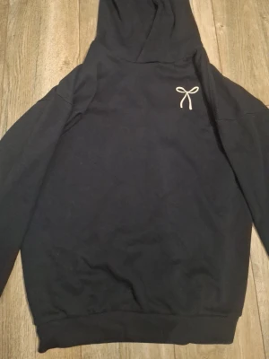 Blå hoodie från Uniq Studio - En superfin hoodie med roseter. Den är mjuk och skön att på sig under en kall höst eller vinterdag. Den är i storleken 158/ 164.