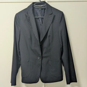 Svart randig kavaj Vogue - Kavaj från Vogue Peek & Cloppenburg med tunna vita ränder. Klassisk modell med två knappar framtill, två stora fickor och helfodrad insida.