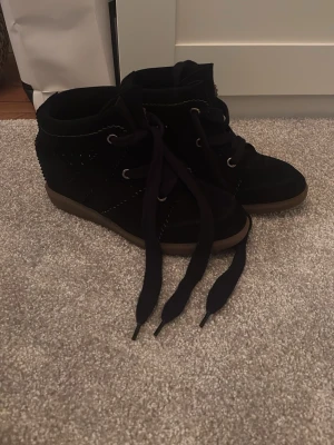 Svarta Isabel marant skor  - Säljer ett par svarta sneakers i mocka med högt skaft och grov brun gummisula. Skorna har snörning med breda svarta skosnören och dekorativa sömmar. Perfekt för dig som gillar en stilren och cool look.