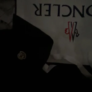 Svart vindjacka från Moncler - Svart vindjacka från Moncler med klassisk logga på ärmen. Jackan har huva med snörning, dragkedja framtill och innerfoder. Snygga detaljer med Monclers signaturfärger i luvan. Perfekt för dig som vill ha en stilren och sportig look.