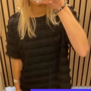 Svart randig topp från H&M - Säljer en svart topp från H&M med horisontella ränder och fransiga kanter. Toppen har rund halsringning och korta ärmar. Den har en boxig passform och är perfekt för dig som gillar en stilren men ändå unik look.