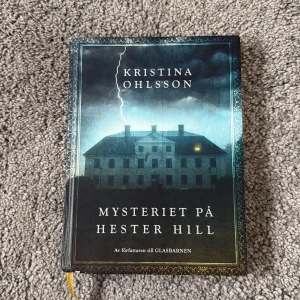 Mysteriet på Hester Hill - En spännande bok med mystisk stämning, perfekt för dig som gillar gåtor och hemligheter. Omslaget visar ett stort hus i mörker med blixtar, och inuti finns en karta över Hester Hill och Svarthhed. Boken lockar med mysterier och äventyr i en suggestiv miljö. Säljer denna bok för 50 kr