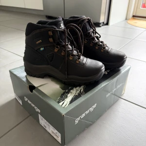 Svarta vandringskängor Graninge strl 38 - Superfina svarta fodrade vandringskängor från Graninge med grov mönstrad sula för extra grepp. Skorna har snörning med metallhakar, bruna detaljer och svensk flagga på sidan. Tillverkade i läder, perfekta för utomhusäventyr. Endast använda en gång, kommer i originalkartongen. Nypris 1799:-, säljer för 1200:-. Pris kan diskuteras. 🩷