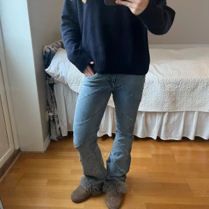 Lågmidjade ljusblå jeans med sned söm - Säljer ett par lågmidjade ljusblå jeans med unika sneda sömmar över benen. Jeansen har klassisk femficksdesign och en lätt utsvängd bootcut-passform. Tillverkade i jeansmaterial och perfekta för dig som gillar en cool och avslappnad stil. Byxorna är lite slitna längst ned.