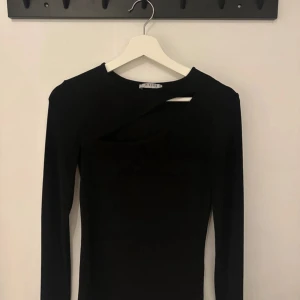 Svart långärmad topp med cut-out från Pieces - Svart långärmad topp från Pieces med cool asymmetrisk cut-out detalj vid halsen. Slim fit och mjukt stretchigt material som sitter snyggt på kroppen. Perfekt för dig som gillar minimalistisk stil med en twist.