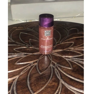 Rituals Shimmering Body Oil - Shimmering body oil från Rituals of Sakura med en lyxig rosa-brun färg och glittrande finish. Kommer i en smidig plastflaska med lila lock, perfekt för att ge huden extra glow och lyster. Innehåller 30 ml.