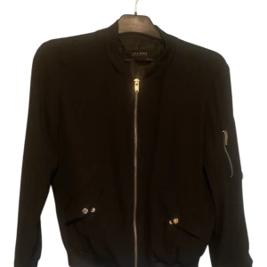 Svart bomberjacka från Zara Basic - Svart bomberjacka från Zara Basic med klassisk siluett, dragkedja framtill och fickor med tryckknappar. Jackan har ribbade muddar och en extra ficka med dragkedja på ärmen. Perfekt för dig som gillar en clean och stilren look.