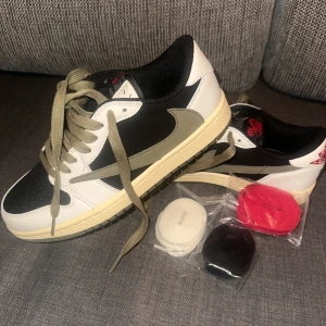 Nike Air Jordan 1 Low Travis Scott - Nike Air Jordan 1 Low Travis Scott med svart, vit och grön färgblock, ikonisk omvänd Swoosh och broderad röd logga på hälen. Skorna har snörning och kommer med extra skosnören i rött, vitt och svart. Stilren och unik design i skinn och syntet. Säljer pgs köpt för stor storlek :/ aldrig använda de A-ko/py