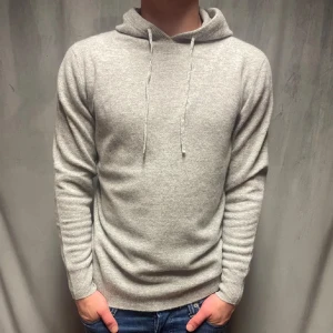 Ljusgrå hoodie i kashmir - Mjuk och stilren ljusgrå hoodie med huva och snörning. Tröjan är stickad i kashmir och har långärmade ribbade muddar. Perfekt för dig som gillar enkel och clean look med lyxig känsla. Passar dig som vill ha en normal passform och diskret vibe.